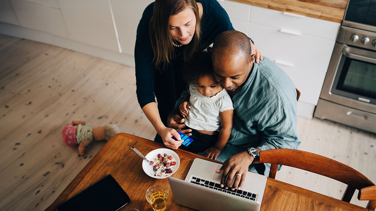 A couple with their child using a laptop in the kitchen.