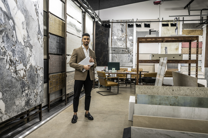 A sales representative in a modern flooring showroom stands confidently holding a tablet among large tile displays.