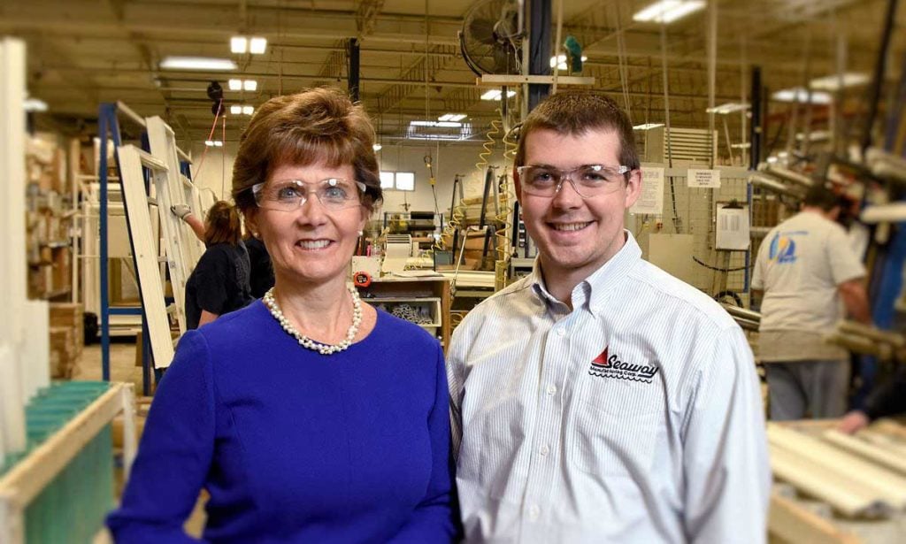 Jana ands Pat Goodrich standing in their manufacturing facility. The woman is wearing a blue top and safety glasses, and the man is wearing a white shirt with a logo and safety glasses.