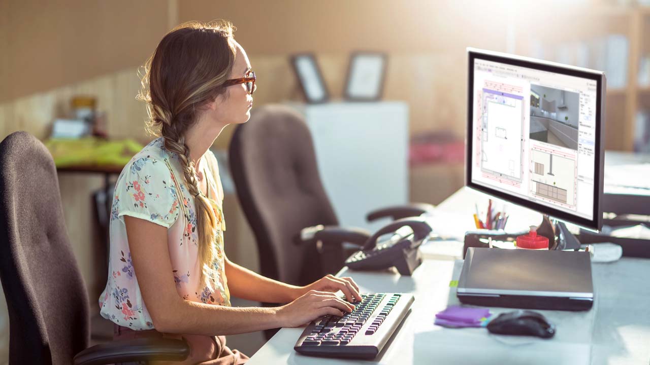 A woman seated at a desk, focused on her computer.