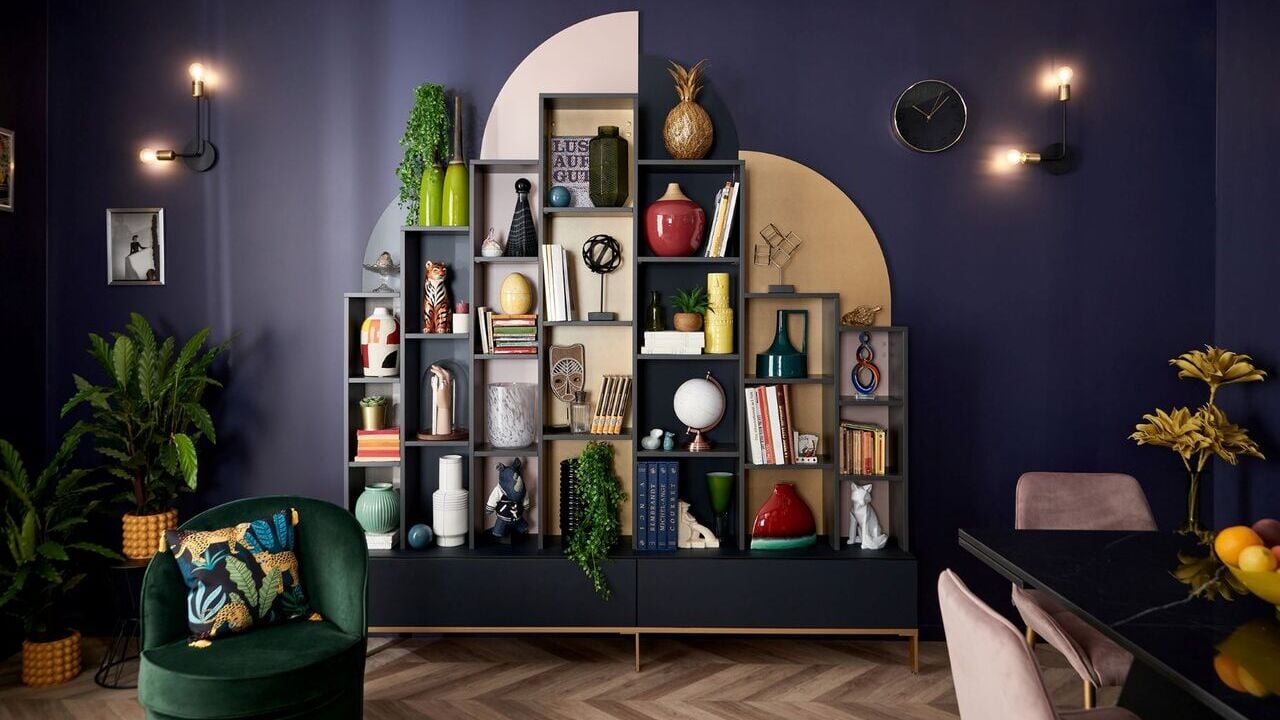 A cozy living room with vibrant purple walls and a stylish bookcase filled with books and decorative items.