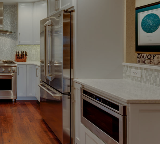 Modern kitchen design with stainless steel appliances, including a refrigerator, oven, and microwave, white cabinetry, and a sleek backsplash, complemented by a wooden floor and decorative wall art.