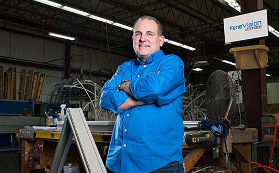 A man wearing a blue shirt stands confidently in a factory setting