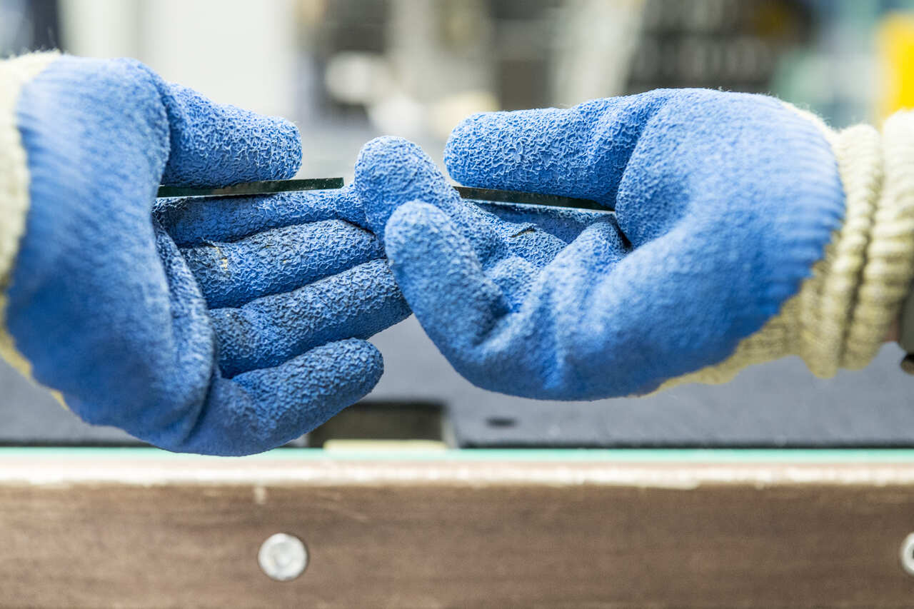 Two hands in blue gloves grasping two pieces of glass