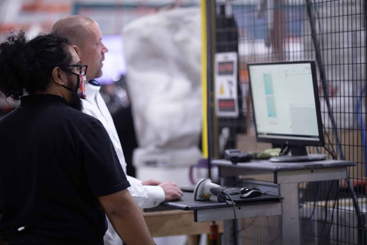 Two men in a factory observe a computer screen