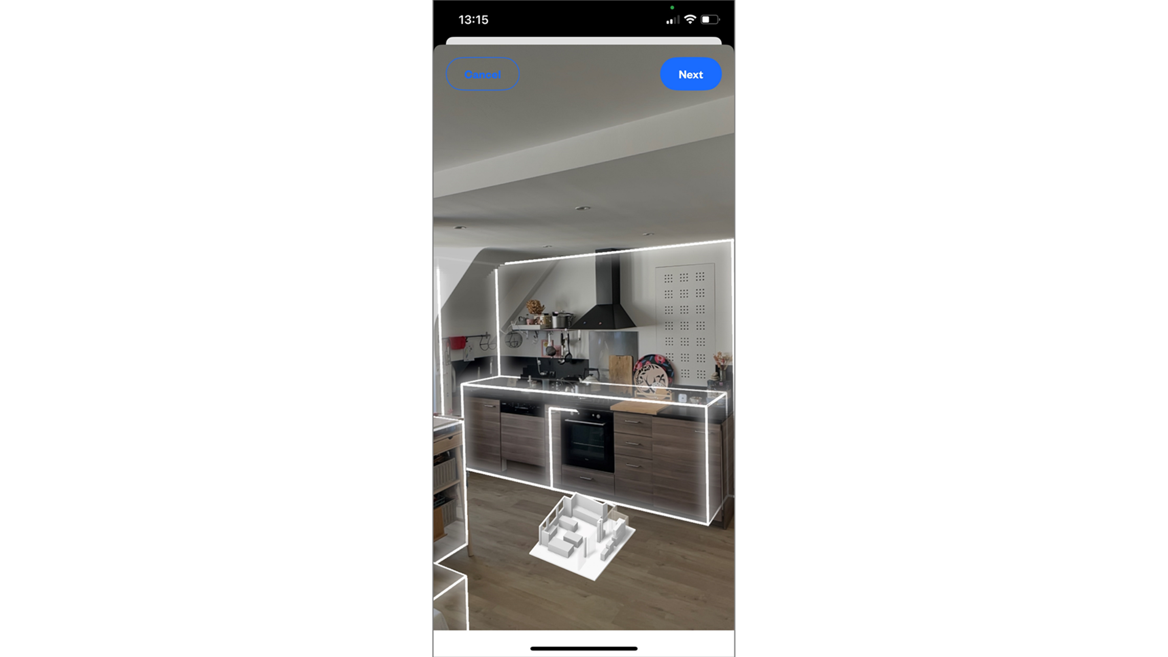 Mobile app interface showing a kitchen being scanned with an augmented reality outline. The room's layout, including cabinets and appliances, is highlighted with white lines, and a 3D model of the scanned room appears at the bottom. The screen includes 'Cancel' and 'Next' buttons, indicating that the scan process is active.